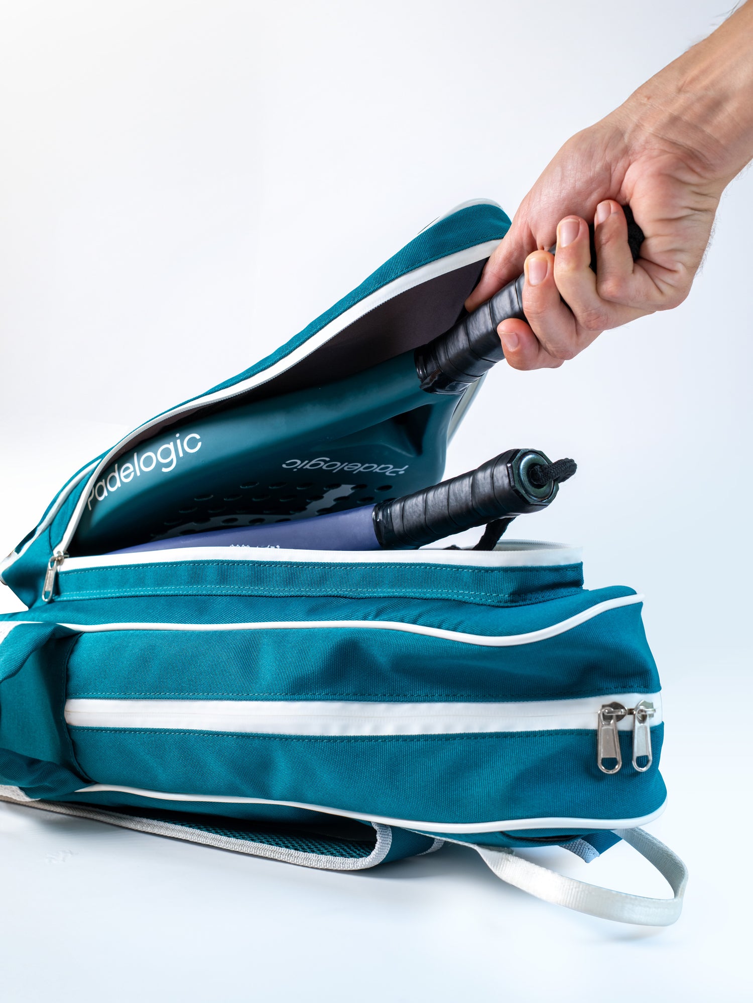 Teal padel racket bag with a hand holding one racket and pressing it against the bag on a white background