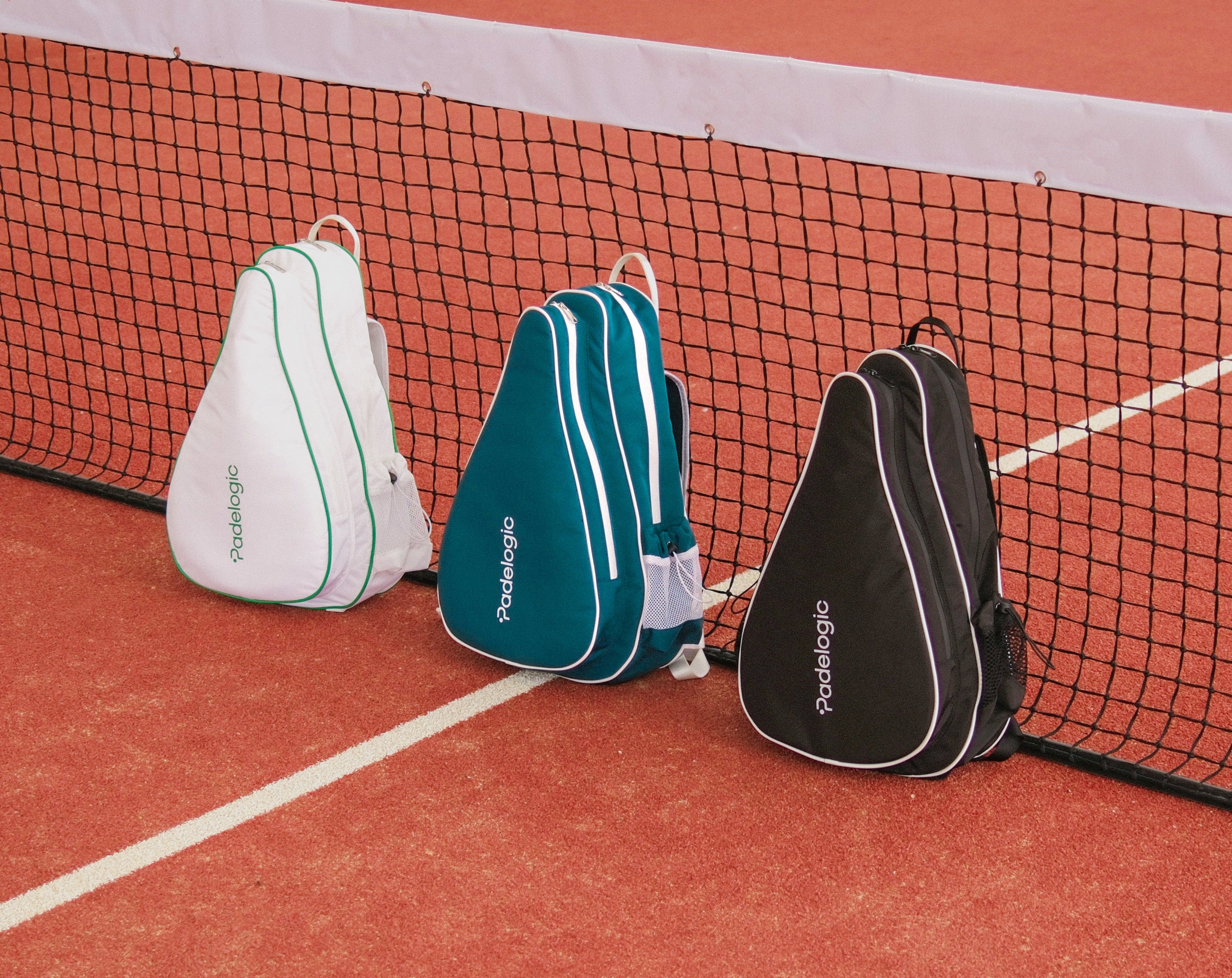 Three padel racket bags on a clay tennis court with a net in the background.